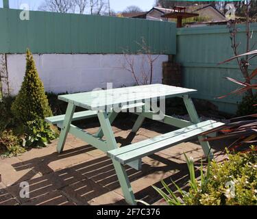 Abgeschiedener Gartensitzbereich mit farbenprächtiger türkisfarbener Picknicktisch an einem hellen und sonnigen Apriltag in Cornwall. Stockfoto