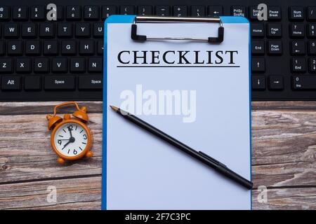 Text auf blauem Klemmbrett auf einer Tastatur mit Wecker und Stift auf Holzschreibtisch Stockfoto