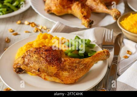Gebratene Hähnchenschenkel mit Kürbiskartoffelpüree und grünen Bohnen Serviert auf einem Teller mit Messer und Gabel in der Küche Tischhintergrund zu Hause Stockfoto