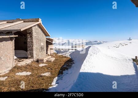 Typische alte Steinkuhschuppen auf Lessinia Plateau im Winter mit Schnee. Gipfel des Corno d'Aquilio. Im Hintergrund der Gipfel des Monte Carega. Venetien, Italien Stockfoto