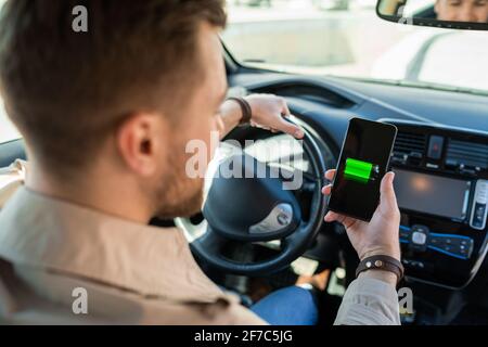 Mann beobachtet Ladeanzeige für Elektroautos über Smartphone-App. Akkustand auf dem Mobiltelefon-Bildschirm Stockfoto