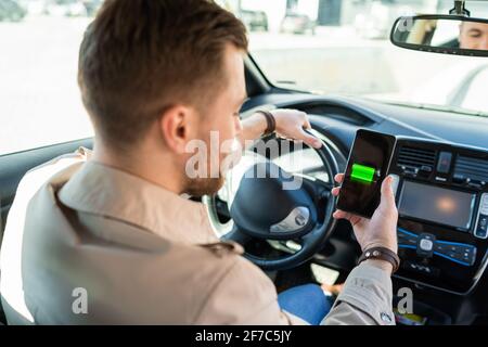 Mann beobachtet Ladeanzeige für Elektroautos über Smartphone-App. Akkustand auf dem Mobiltelefon-Bildschirm Stockfoto