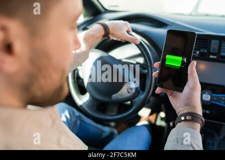 Mann beobachtet Ladeanzeige für Elektroautos über Smartphone-App. Akkustand auf dem Mobiltelefon-Bildschirm Stockfoto