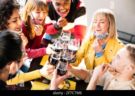 Glückliche Freunde tragen schützende Gesichtsmasken toasting Rotwein sitzen Im Restaurant - Neues normales Freundschaftskonzept mit jungen Menschen Viel Spaß im ho Stockfoto