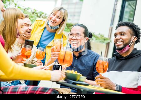 Multirassische Freunde, die Gesichtsmasken tragen, trinken Cocktails im Bar-Restaurant - Neues normales Freundschaftskonzept mit jungen Leuten, die das Essen genießen Im Hintergrund Stockfoto