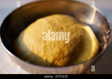 Backkonzept, Kuchen oder Ostergebäck. Frisch zubereiteter Brotteig in der Küche in Edelstahlschüssel bei Sonnenuntergang. Hochwertige Fotos Stockfoto