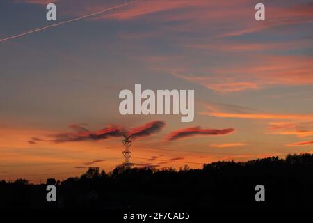 Märchenhafte Sonnenuntergangslandschaft mit orangefarbenen, rosa und violetten Wolken. Scheint wie ein Sonnenuntergang gemalt zu sein. Heller und magischer Sonnenuntergang über dunklen Hügeln. Stockfoto