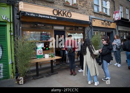 London, England, Großbritannien. Hackney. London Fields. Broadway Market. Junge Menschen auf der Straße warten auf Take-away vor Okko, Japan und Pazifik Stockfoto