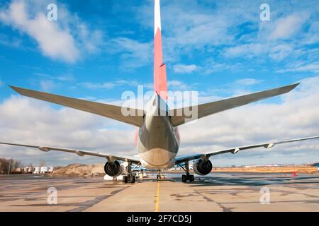 Das Flugzeug parkte am Flughafen vor dem Hintergrund eines blauen Himmels mit Wolken, Rückansicht Stockfoto