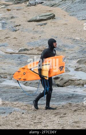 Ein männlicher Surfer, der bei Little Fistral über den Strand läuft und ein gebrochenes Surfbrett in Newquay in Cornwall trägt. Stockfoto