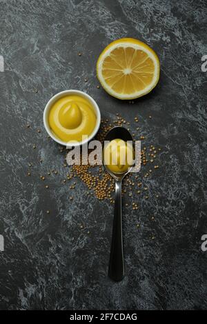 Schüssel und Löffel mit Senf, Samen und Zitrone auf schwarzem rauchigen Hintergrund Stockfoto