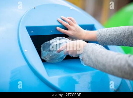 Abfallsortierung. Weibliche Hand werfen Plastiktüte in blauen Papierkorb im Freien Stockfoto