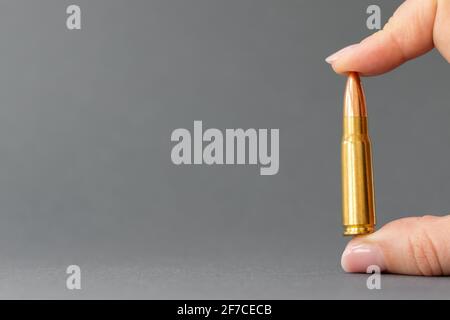 Hand mit Kugel auf grauem Hintergrund. Patrone Kaliber 7.62 für Kalaschnikow Sturmgewehr in den Fingern Nahaufnahme mit Kopierraum. Stockfoto