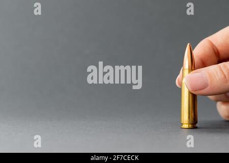 Hand mit Kugel auf grauem Hintergrund. Patrone Kaliber 7.62 für Kalaschnikow Sturmgewehr in den Fingern Nahaufnahme mit Kopierraum. Stockfoto