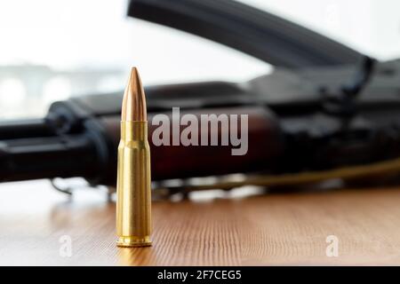 Eine Kugel gegen verschwommenes Kalaschnikow-Sturmgewehr im Hintergrund. Cartridge 7.62 Kaliber für ak 47 Closeup. Stockfoto