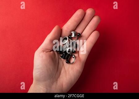 Piercing und Schmuck für die Ohren in der Handfläche Die Hand auf einem roten Hintergrund Draufsicht Stockfoto