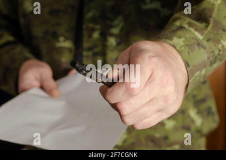 Ein Offizier hält einen schwarzen Stift an die Kamera. Eine Männerhand bietet einen Stift an, um ein Dokument zu unterschreiben. Mann mittleren Alters. Selektiver Fokus. Low-Taste. In Innenräumen Stockfoto