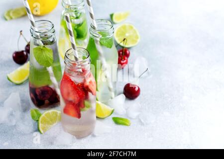 Flaschen Limonade erfrischende Sommerlimonade mit Limette, Erdbeere, Kirsche, Gurke und Eis auf grauem Betongrund. Modell. Stockfoto