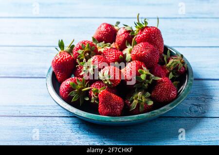 Frische Erdbeeren in Grün auf Blau Holztisch mit schönen Reflexionen und Schatten Stockfoto