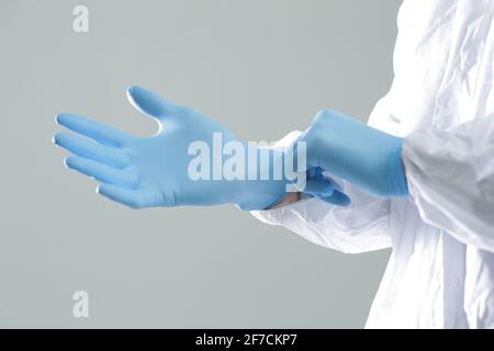 Der Arzt in einem Schutzanzug zieht blaue Gummihandschuhe an Stockfoto