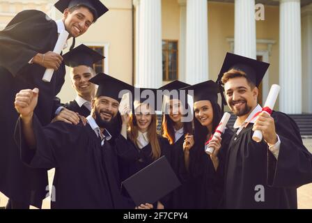 Gruppe von Absolventen in schwarzen Roben mit Diplomen in den Händen Nach der Abschlussfeier Stockfoto