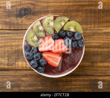 Brasilianische typische acai Schale mit Kiwi, Heidelbeere und Erdbeere über Holztisch. Stockfoto