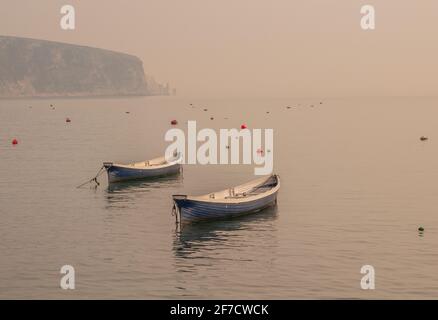 Zwei leere blaue Ruderboote spiegeln sich in einer ruhigen, nebligen, nebligen Dorset, Swanage Bay Stockfoto