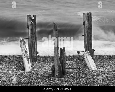Die zerstörten, symmetrisch umrahmten Meeresverteidigungen standen an einem Kiesstrand vor rollenden Breakern, die sich in kubistische, abstrakte Geister verwischten. Stockfoto