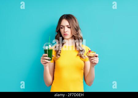 Unglückliche Frau bei der Diät, die nach Smoothie sucht, indem sie zwischen Detox-Saft und Süßigkeiten wählt. Diät-Konzept. Gesunde Ernährung Lebensstil Stockfoto