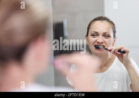 Eine junge Frau putzt sich im Badezimmer vor der Tür die Zähne Spiegel Stockfoto