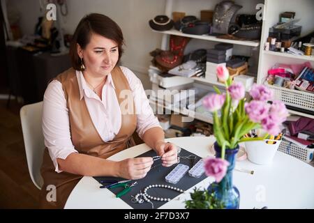 Nachdenkliche, ruhige, dunkelhaarige Kunsthandwerkerin, die in ihrem Atelier sitzt Stockfoto