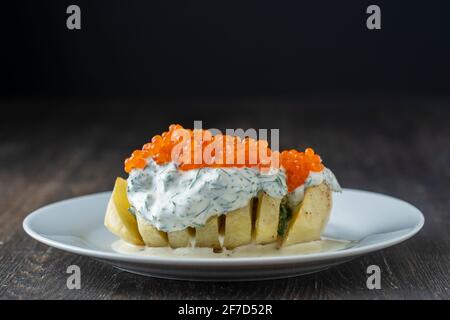 Gebackene Kartoffel mit cremiger Käsesauce, gewürzt mit Dill und rotem Lachskaviar auf weißem Teller, Nahaufnahme Stockfoto