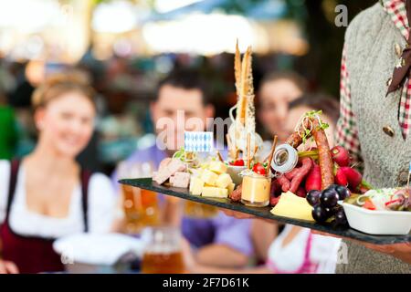 Im Biergarten - Freunde Tracht, Dirndl und auf einem Tisch mit Bier und Snacks in Bayern, Deutschland Stockfoto