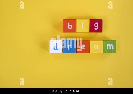 Wörter großer Traum aus farbigen Holzblöcken. Sie sind in zwei Reihen angeordnet. Bemalte Würfel mit Buchstaben auf gelbem Hintergrund. Draufsicht Stockfoto