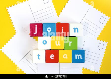 Wörter Join our Team made from colored wooden Blocks. Sie sind in drei Reihen angeordnet. Bemalte Würfel mit Buchstaben auf gelbem Hintergrund. Stockfoto