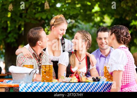 Im Biergarten - Freunde Tracht, Dirndl und auf einem Tisch mit Bier und Snacks in Bayern, Deutschland Stockfoto