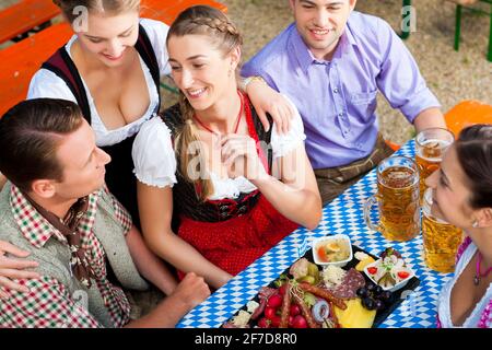 Im Biergarten - Freunde Tracht, Dirndl und auf einem Tisch mit Bier und Snacks in Bayern, Deutschland Stockfoto