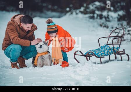 Familienspaziergang im Winterwald mit Huskies, glücklicher Tochter und Papa, die mit einem Hund spielen. Neujahrswanderung durch den Märchenwald. Stockfoto