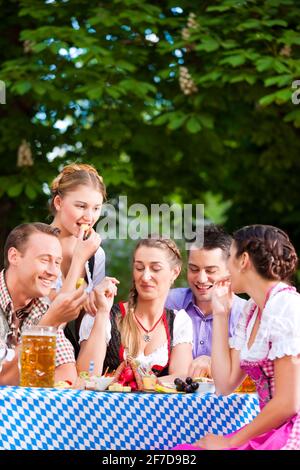 Im Biergarten - Freunde Tracht, Dirndl und auf einem Tisch mit Bier und Snacks in Bayern, Deutschland Stockfoto