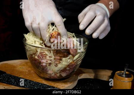 Ein großes Stück Schweinefleisch wird in Stücke geschnitten, vom Koch mit Gewürzen mariniert, und der Koch reibt die Kartoffeln auf einer Reibe zur Marinade.2020 Stockfoto