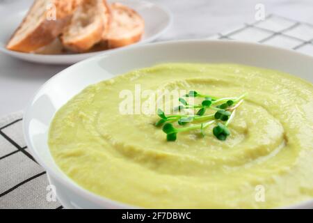 Nahaufnahme der klassischen französischen Vichyssoise-Sahnesuppe - Kartoffel-Lauch-Suppe mit Mikrogemüse in einer weißen Schüssel gekrönt Auf Marmortisch Hintergrund und Stockfoto