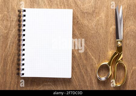 Schneiderschere oder Nähschere und Notizbuch auf Holztischhintergrund, flache Lay Draufsicht Stockfoto