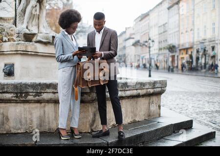 Schöne afro amerikanische Frau zeigt einige Arbeitsinformationen in der Zwischenablage zu schönen Geschäftsmann in Anzug. Konzept der Zusammenarbeit und Unterstützung. Stockfoto