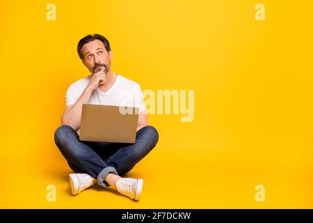 Foto in voller Größe von ernsthaft denkenden Mann sitzen Bodenhalt Laptop sehen leer aus, isoliert auf gelbem Hintergrund Stockfoto