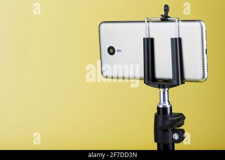 Smartphone auf einem Stativ auf gelbem Hintergrund befestigt. Selfie- und Blogging-Konzept Stockfoto