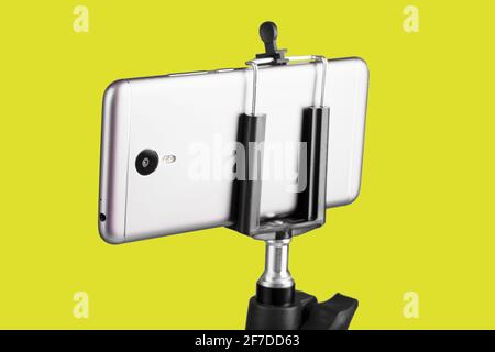 Smartphone auf einem Stativ auf gelbem Hintergrund befestigt. Selfie- und Blogging-Konzept Stockfoto