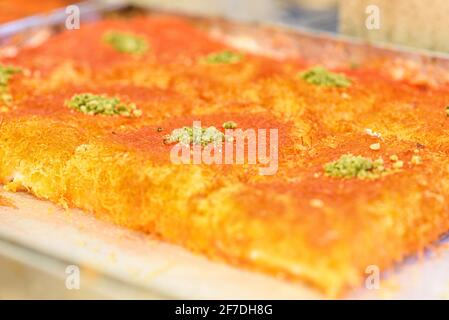 Süßes arabisches Dessert Kunefe, Kunafa, Kadayif mit Pistazien-Pulver und Käse auf dem Tablett auf dem Markt. Stockfoto