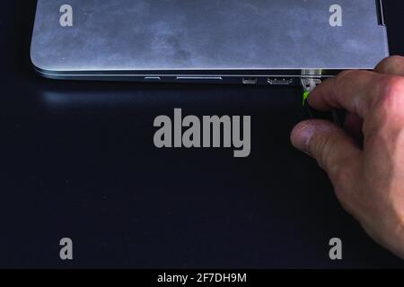 Nahaufnahme der Hand, die das usb-Flash-Laufwerk mit dem silbernen Notebook-Computer verbindet, isoliert auf schwarzem Hintergrund. Stockfoto