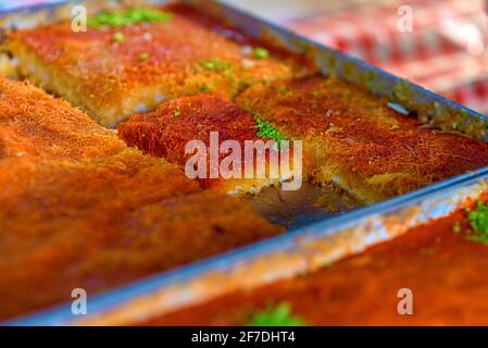 Süßes arabisches Dessert Kunefe, Kunafa, Kadayif mit Pistazien-Pulver und Käse auf dem Tablett auf dem Markt. Stockfoto