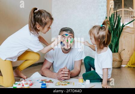 Kinder haben Spaß mit ihrem Vater. Mädchen zeichnen mit bunten Farben auf die Haut eines Mannes. Kreativität und Fantasie. Vatertag und der Co Stockfoto